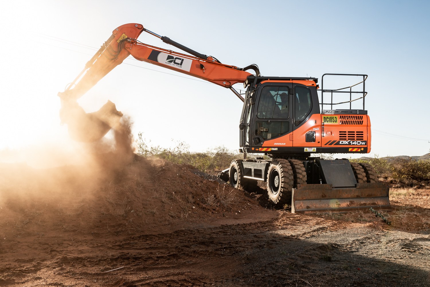 Excavator working in dust backlit by the sun
